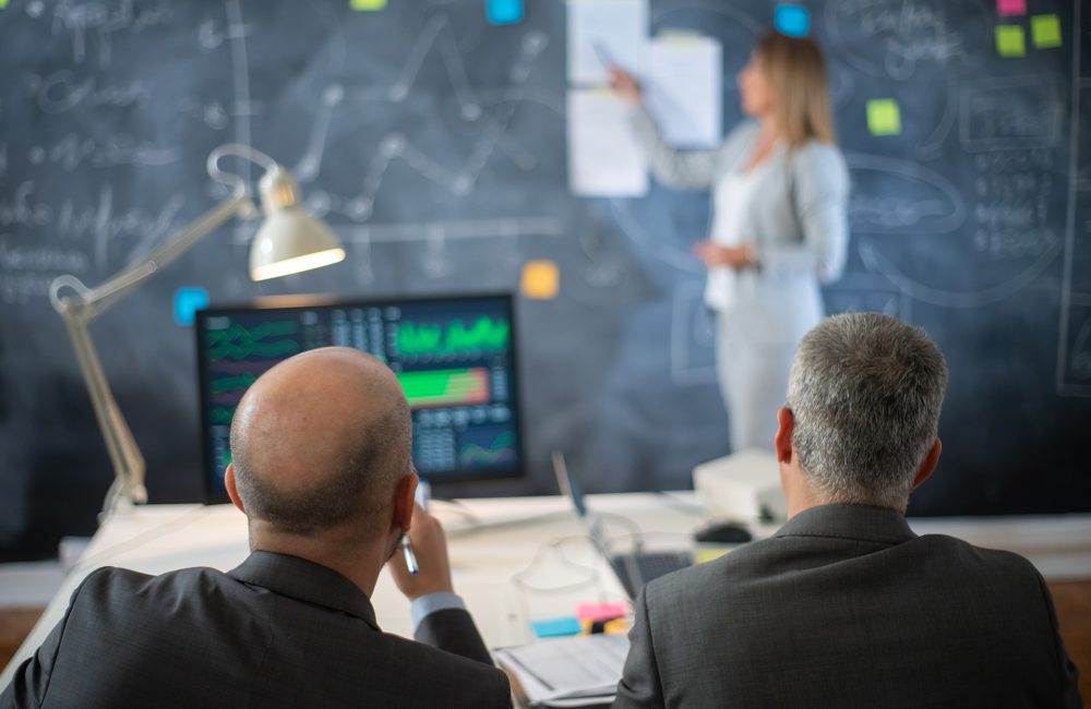 back-view-company-experts-working-office-two-serious-man-formalwear-sitting-looking-woman-presenting-business-plan-market-data-board-financial-analytics-business-growth-concept